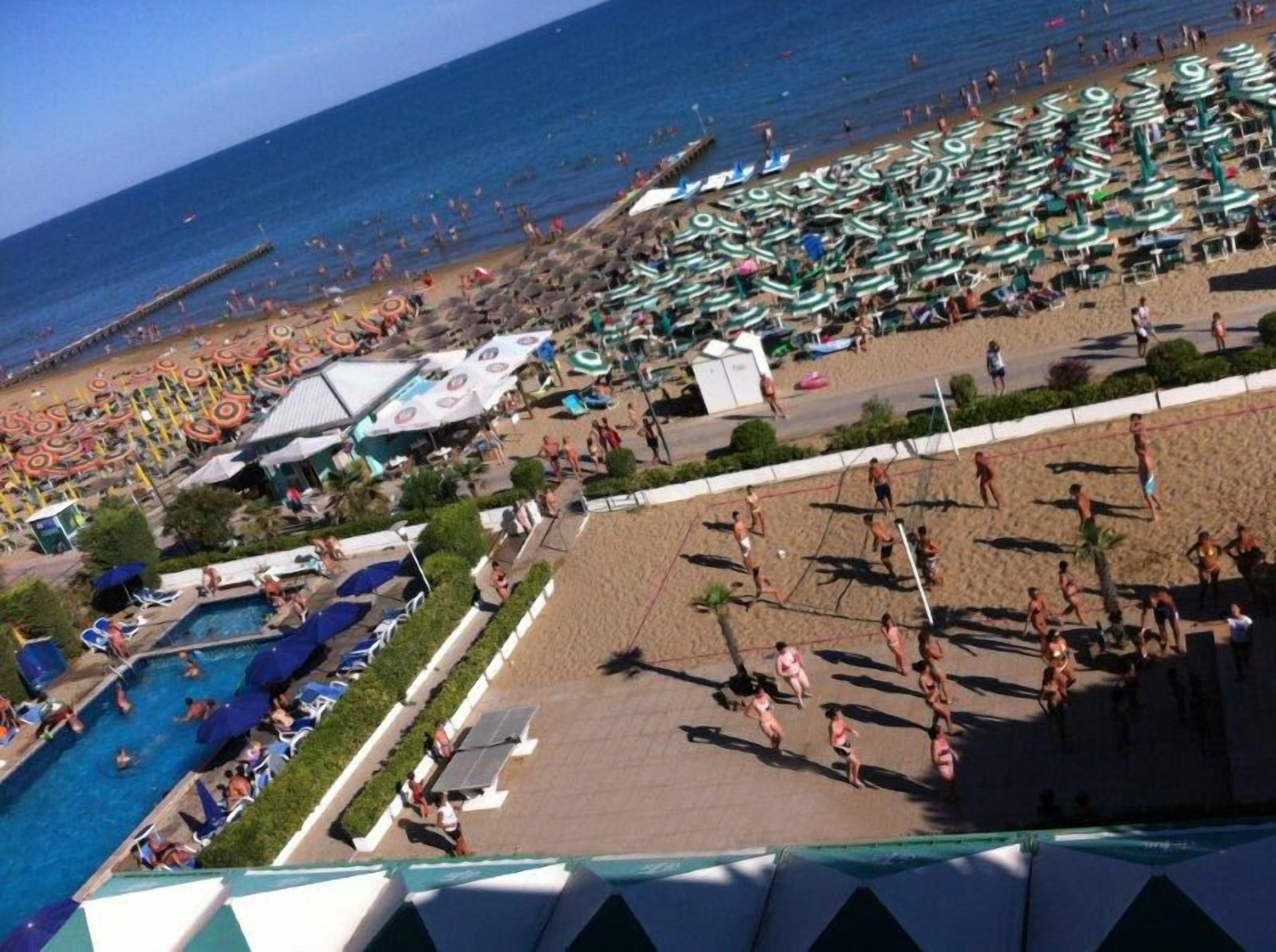 En badehotel med flere swimmingpools, strandparasoller og en volleyballbane.