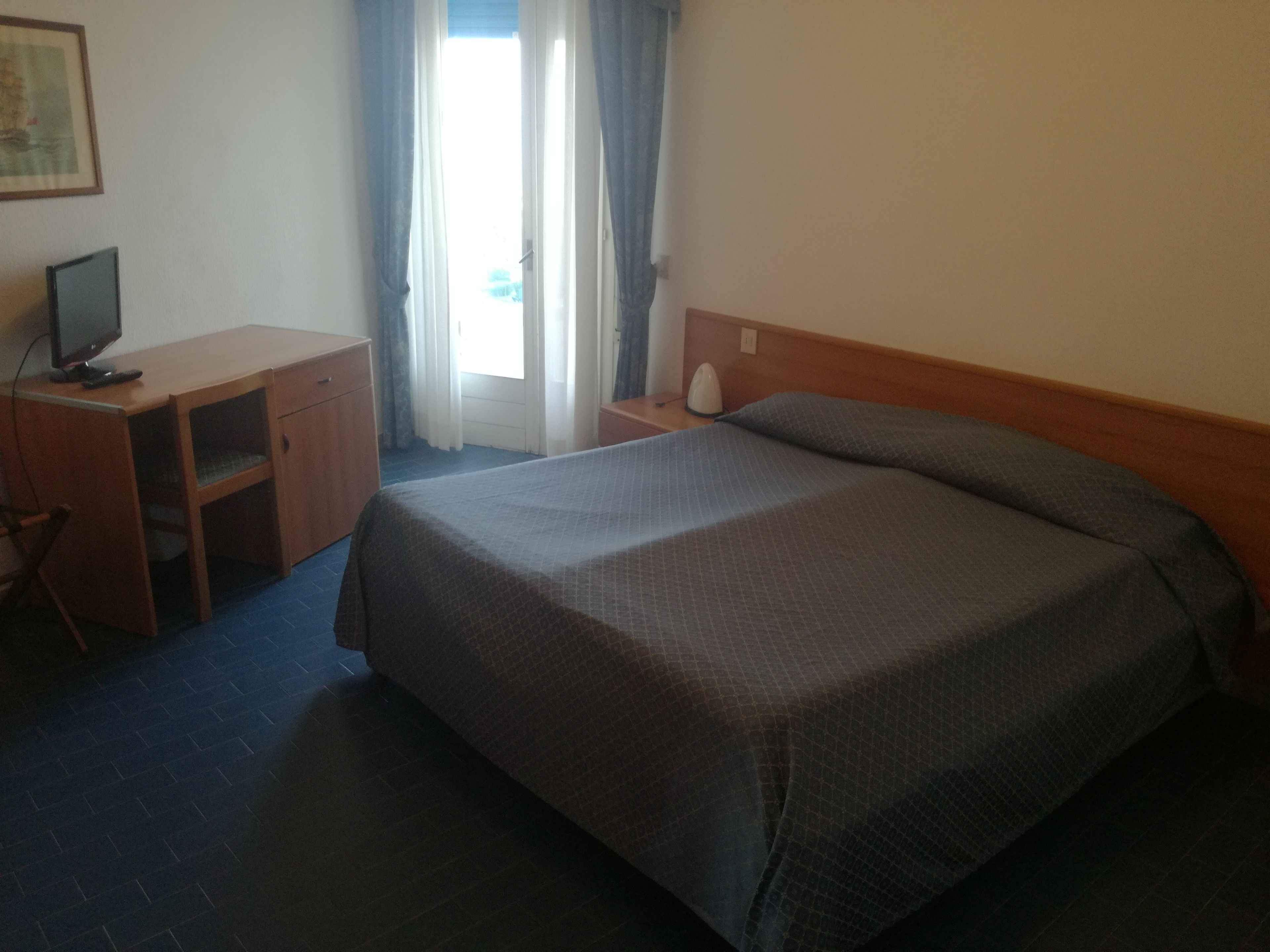 A hotel room with a bed, a desk, a chair, a computer, and a window with curtains.