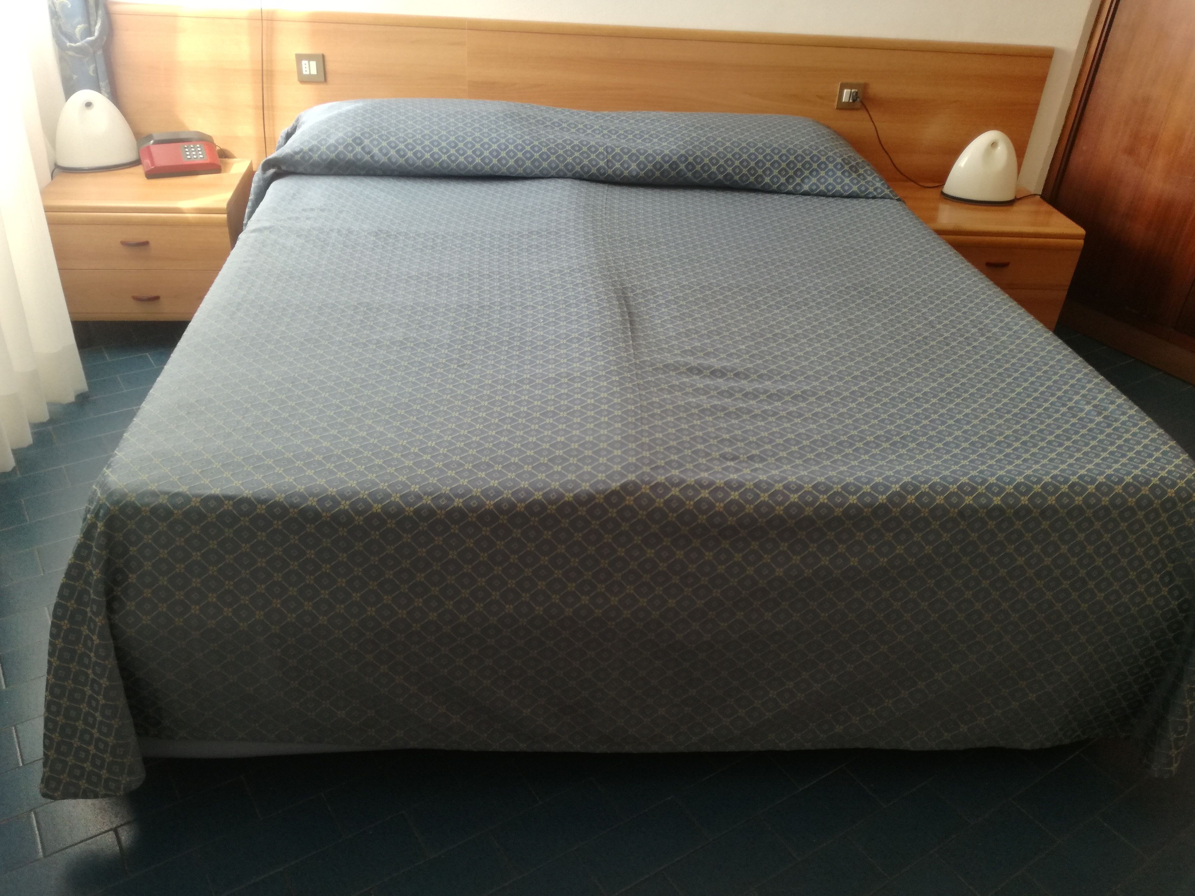 A neatly made bed with a patterned bedspread, a wooden headboard, and bedside tables with lamps.
