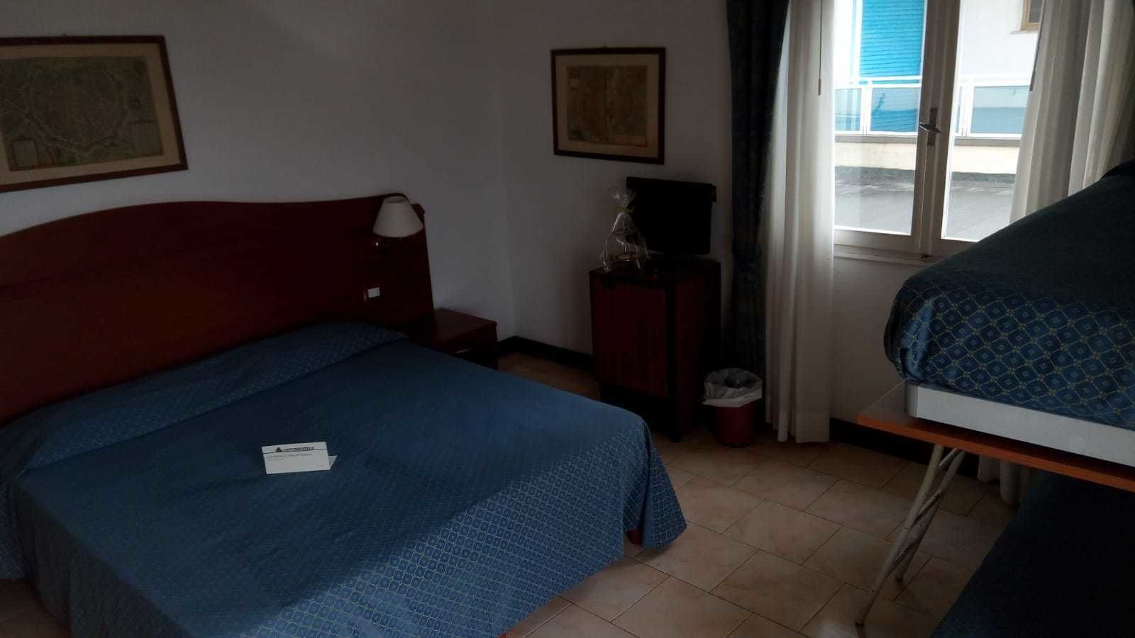 Une chambre d’hôtel équipée d’un lit, d’un bureau, d’une chaise, d’une poubelle et d’une fenêtre avec des rideaux.