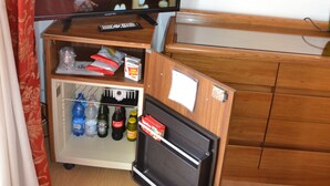 A compact hotel room with a television on a stand, a small refrigerator stocked with beverages, a wooden dresser, and a bed with a patterned bedspread. - Park Hotel Ravenna (Ravenna)