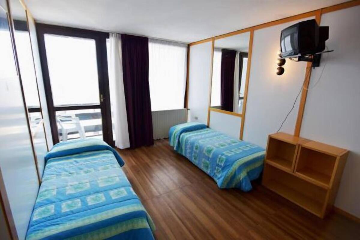 A compact room with two beds, a television mounted on the wall, and a wooden shelf.