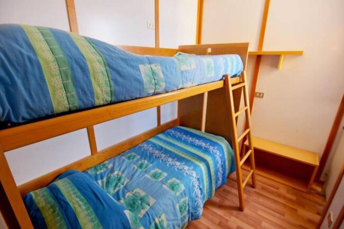 A bunk bed with a ladder, wooden walls, and a shelf.