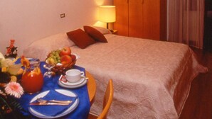 Una habitación de hotel con una cama bien hecha, una mesita de noche con una lámpara y una mesa con artículos de desayuno.