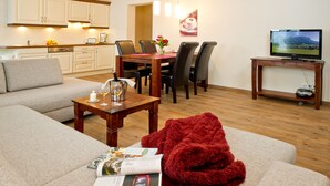 Una sala moderna con un sofá, una mesa de centro con revistas, una manta roja y una zona de comedor con una mesa de madera y sillas.