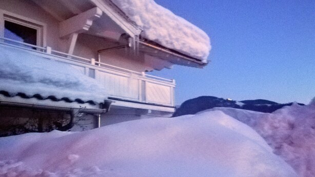 Un balcón cubierto de nieve con una casa al fondo.