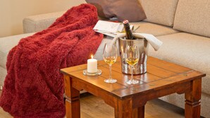 Una sala de estar acogedora con una mesa de centro de madera, una manta roja, una vela encendida y una botella de champán en un cubo.