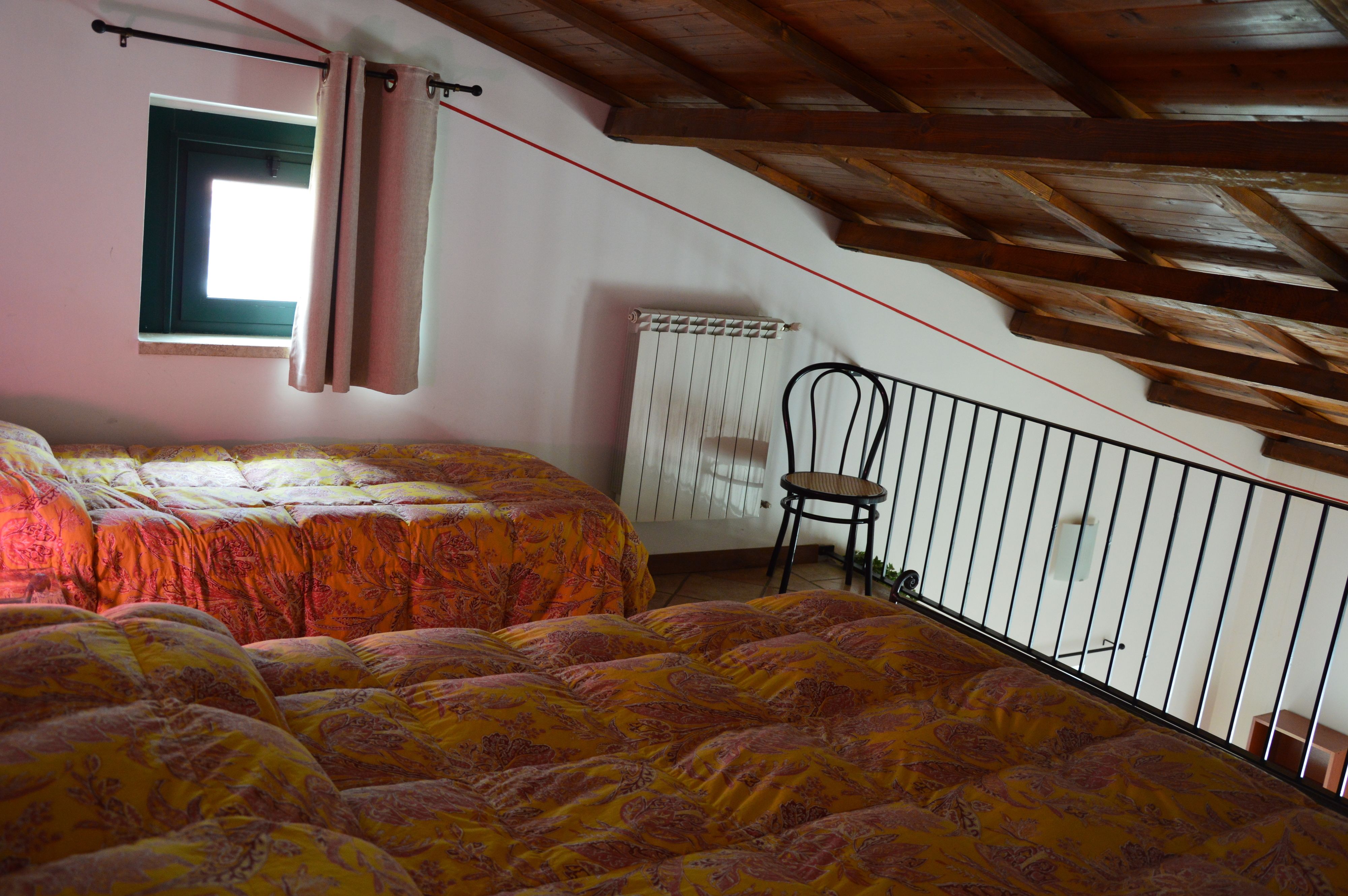 Una camera da letto con due letti, una finestra con tende, un termosifone e una sedia.