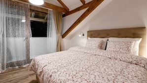 Un dormitorio con techo inclinado, una cama con ropa de cama floral, una ventana con cortinas y una lámpara fijada a la pared.