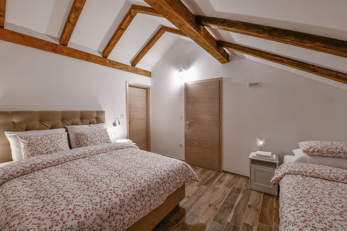 Une chambre dotée d’un grand lit, d’une armoire, d’une table de chevet et d’un plafond avec des poutres apparentes.