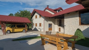 Una casa de dos pisos con techo rojo, fachada de piedra y un banco de madera al frente.