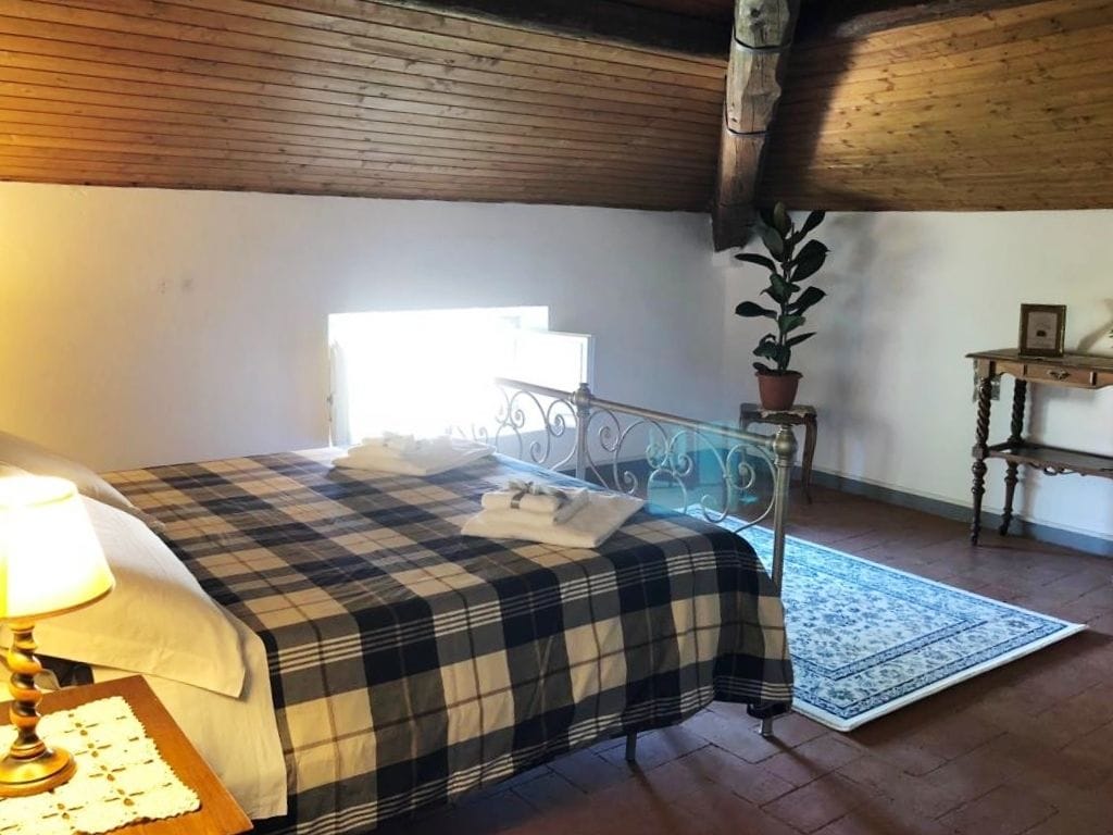 Quarto com colcha xadrez, abajur, planta em vaso e teto de madeira.