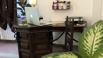 Un bureau en bois avec un ordinateur portable, une plante en pot et une petite étagère ornée d’objets décoratifs.