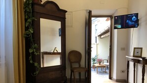 A hotel room with a large mirror, a bed with neatly folded towels, a wooden chair, a small table with a plant, and a television mounted on the wall. - Relais Puccini (Lucca)