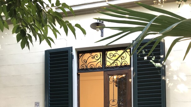 A house entrance with a wooden door, green shutters, and two potted plants on the steps. - Relais Puccini (Lucca)