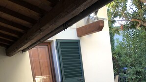 An outdoor patio with a wooden table and chairs, a potted plant, and a door with shutters. - Relais Puccini (Lucca)