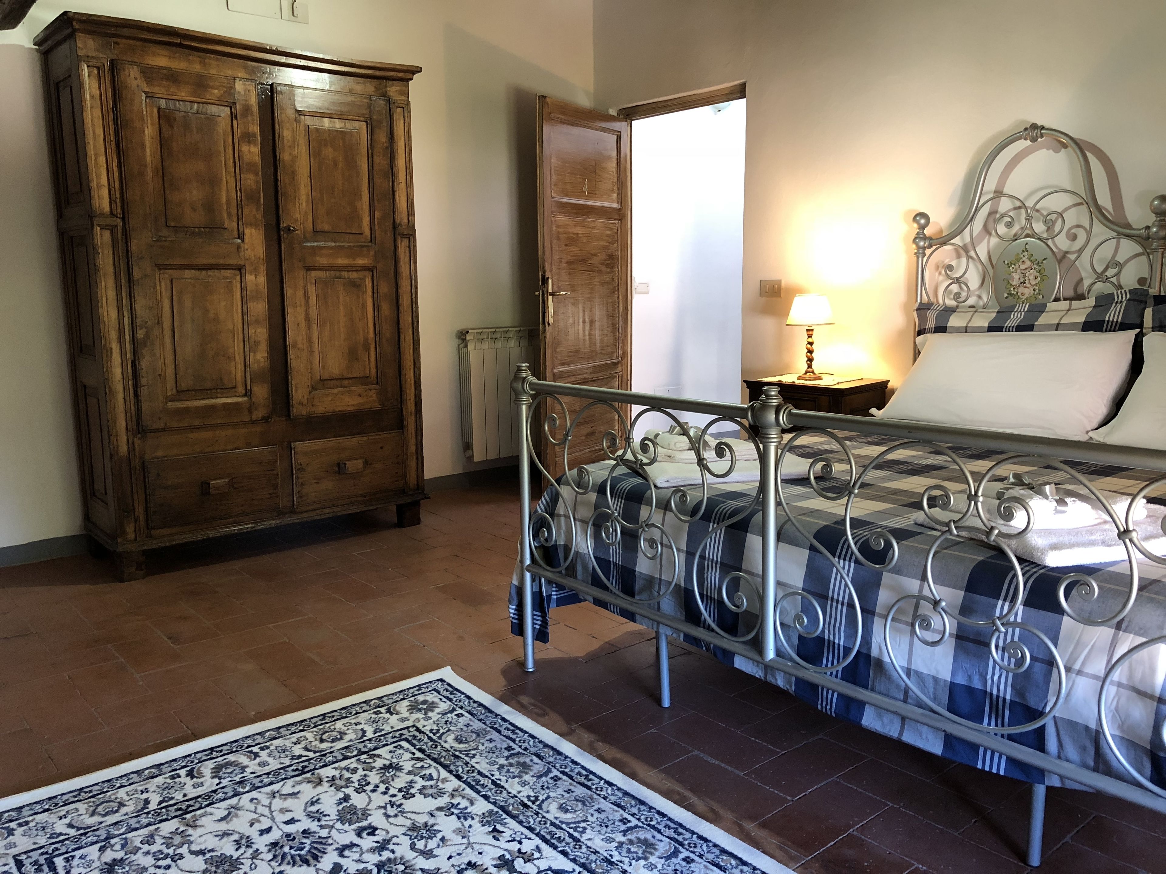 A bedroom with a metal bed frame, a wooden wardrobe, and a patterned rug.