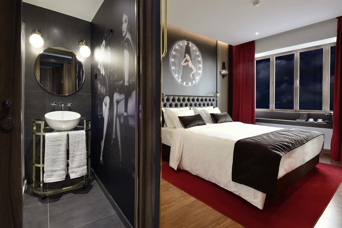 A modern bedroom with a large bed, a round mirror, and a bathroom with a sink and towel rack.