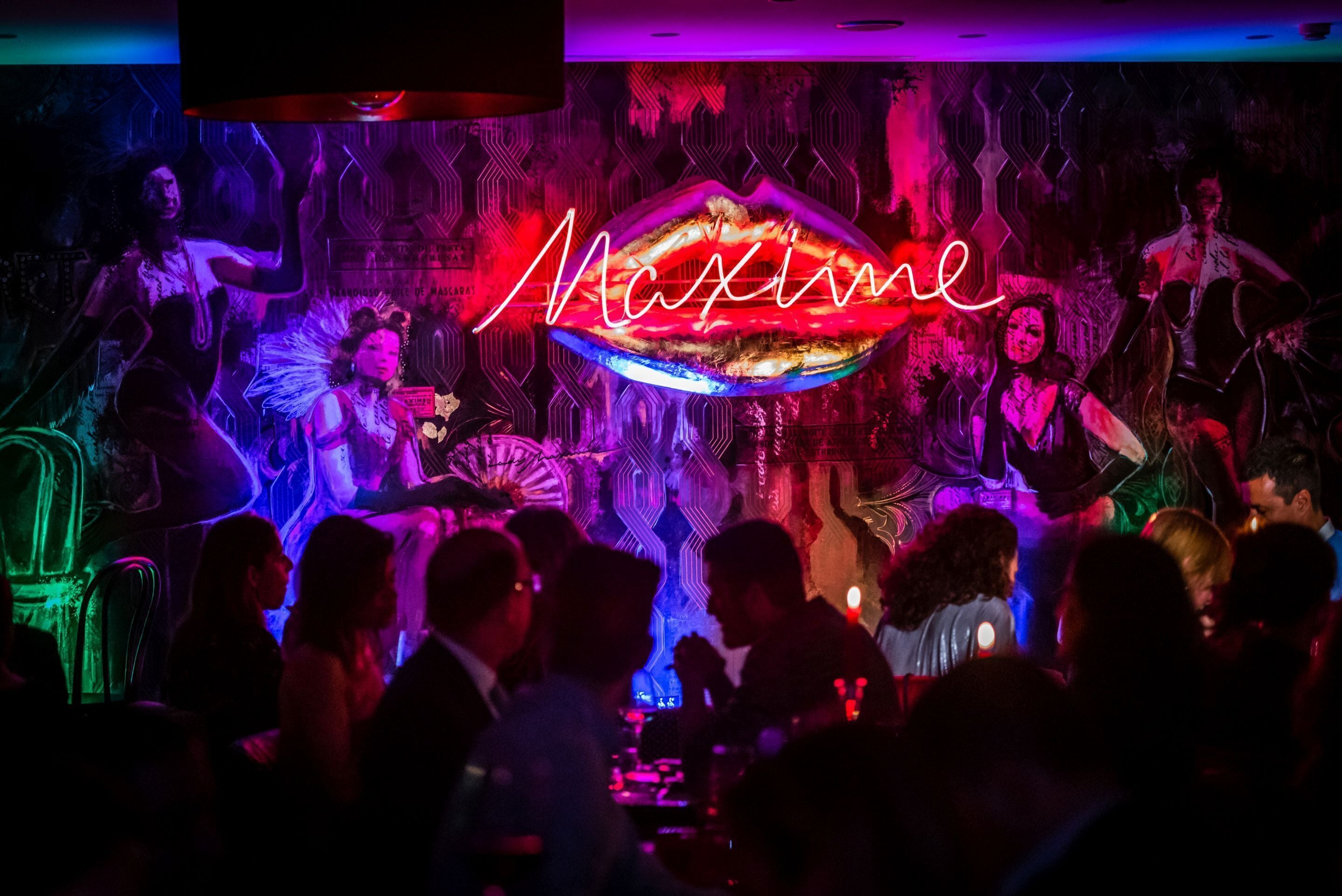 Un bar bondé, avec des enseignes au néon et un mur orné de motifs.