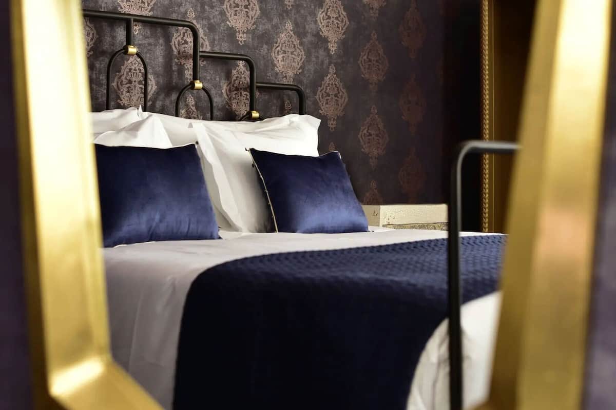 A neatly made bed with a dark blue bedspread and pillows, a white comforter, and a headboard with a decorative pattern.