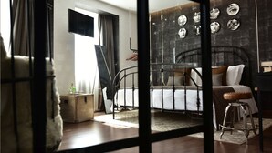 Ein Schlafzimmer mit einem Metallbettgestell, einem hölzernen Hocker, einem kleinen runden Tisch und einem an der Wand befestigten Fernseher.