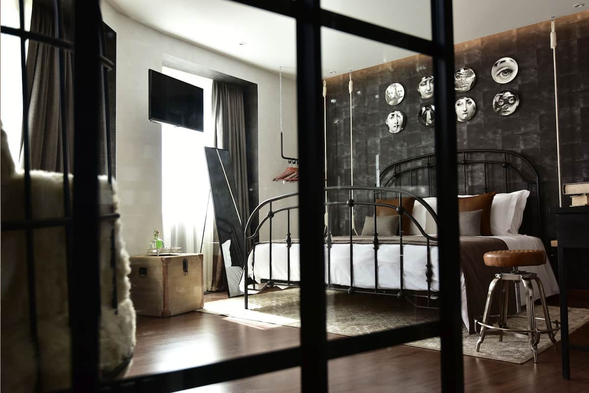 A bedroom with a metal bed frame, a wooden stool, a small round table, and a wall-mounted TV.