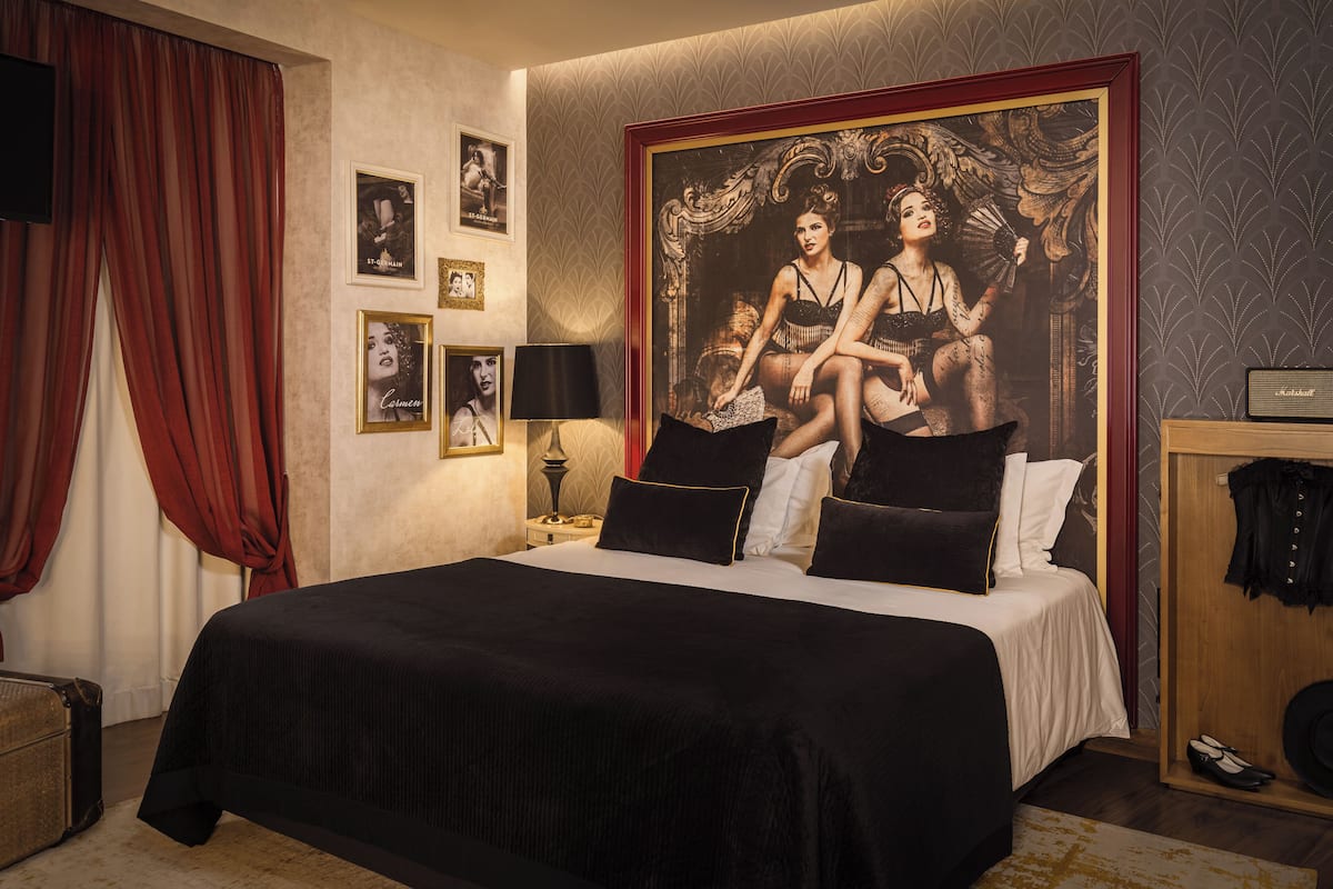 A hotel room with a large bed, a wardrobe, a nightstand with a lamp, and a large framed picture on the wall.