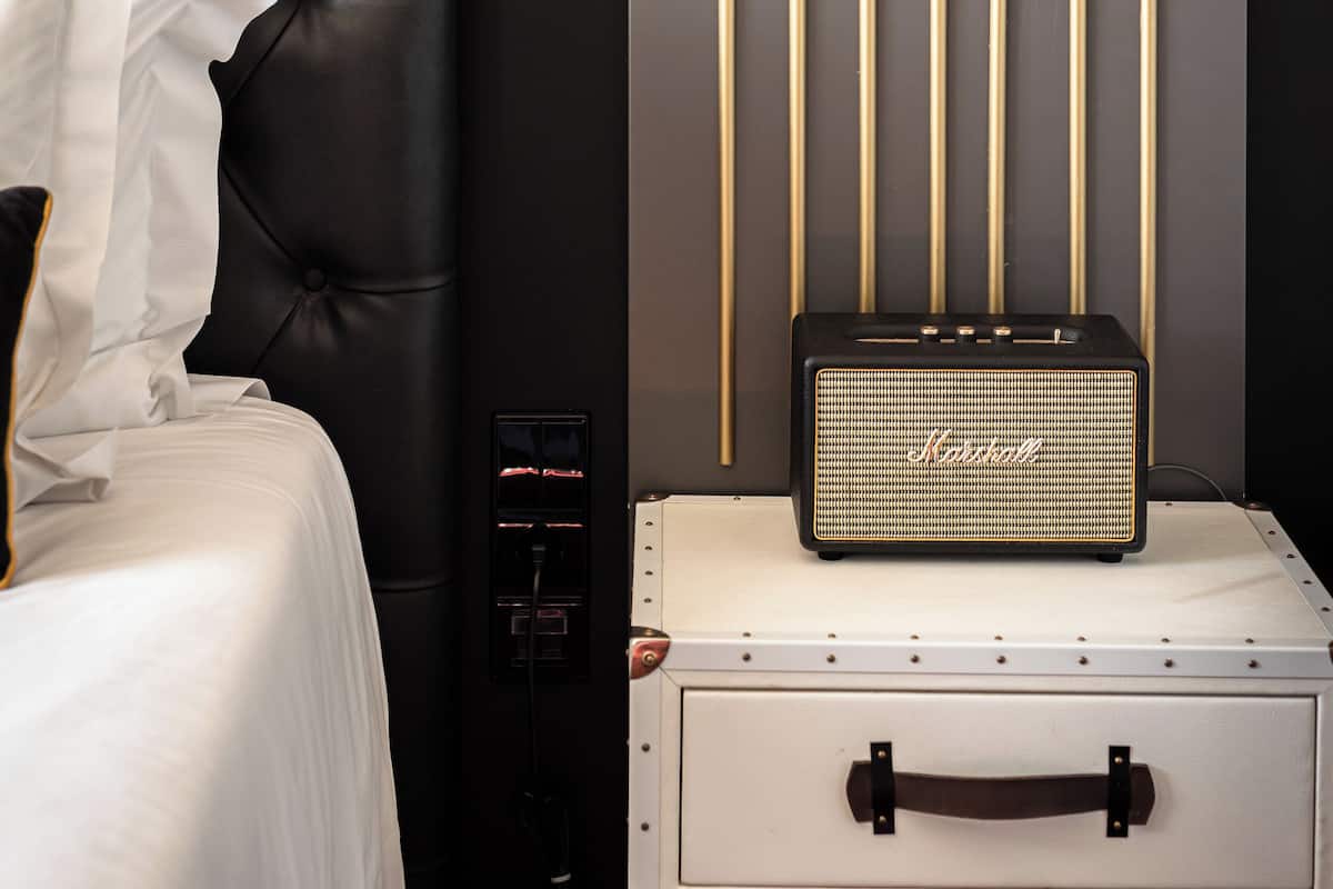 A hotel room with a tufted headboard, a white bed, and a vintage-style radio on a white cabinet.