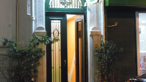 A building entrance with a green door, a sign above it, and a closed shutter to the right. - Zeus Hostel (Athens)