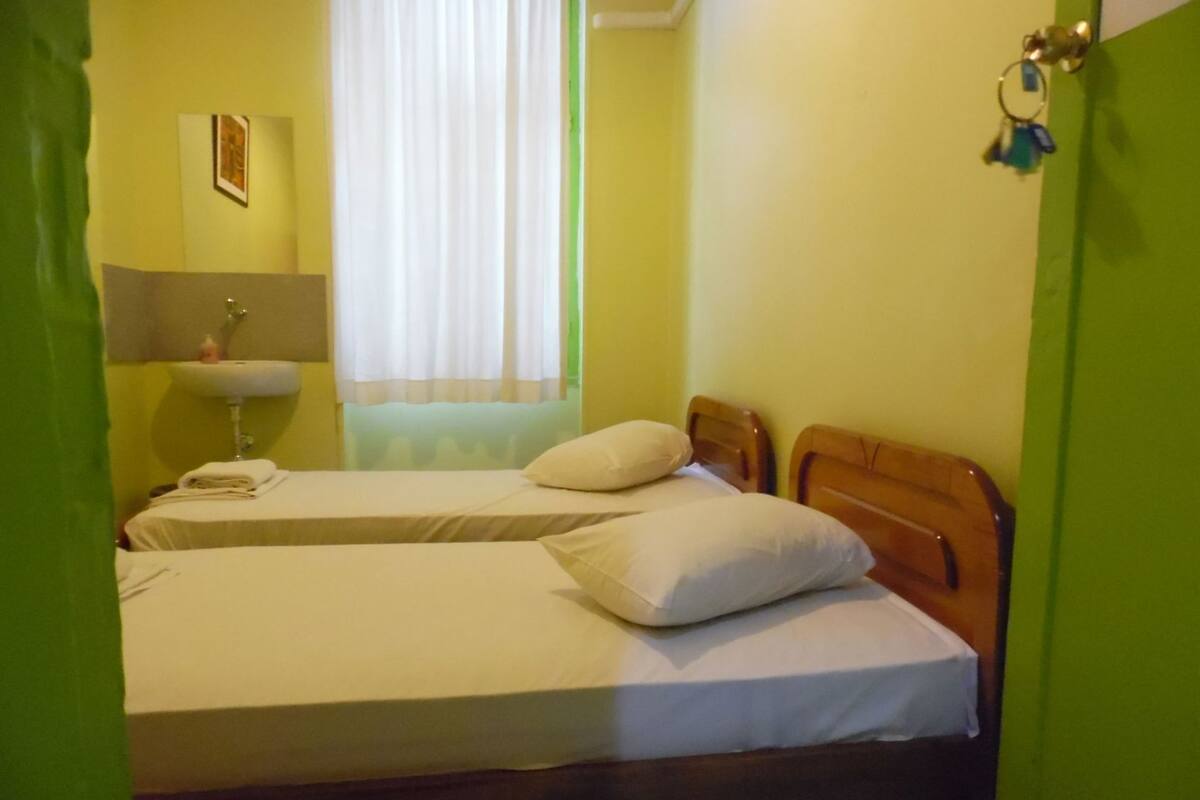 Habitación con dos camas, un lavamanos y una ventana con cortinas.