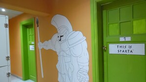 A hallway with green doors, one labeled "THIS IS SPARTA". - Zeus Hostel (Athens)
