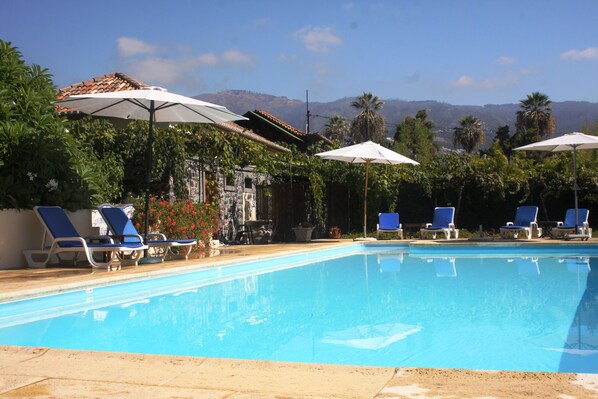 A swimming pool with blue water, surrounded by lounge chairs and umbrellas, with a mountain view in the background. - Casa do Feitor (Funchal)