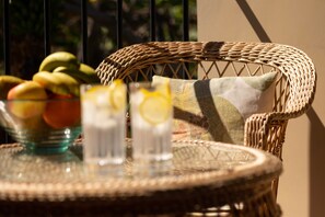 A wicker chair with a cushion, a glass table with a bowl of fruit and two glasses of a beverage with lemon slices. - Casa do Feitor (Funchal)