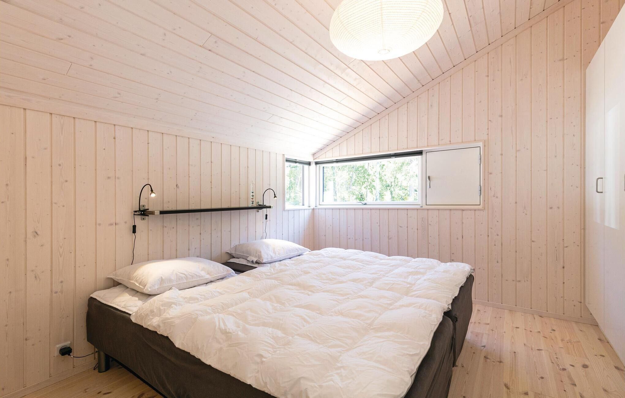 Een slaapkamer met een groot bed, houten wanden, een raam en een plafondlamp.