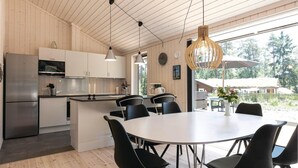 Una cocina moderna con paredes de madera, un refrigerador de acero inoxidable y una zona de comedor con una mesa redonda y sillas negras.