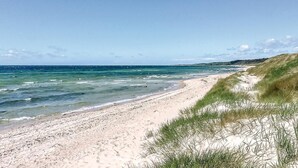 Una playa arenosa con olas suaves, dunas cubiertas de hierba y un cielo despejado.