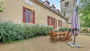 Un bâtiment de style rustique doté d’une terrasse en gravier, de meubles en bois et d’un parasol.