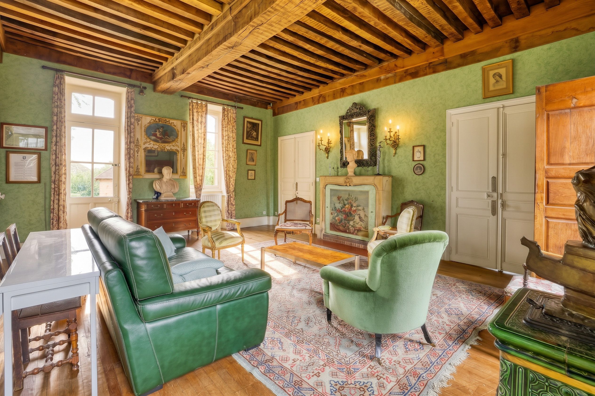Une pièce avec un canapé vert, un fauteuil vert, une table basse en bois, une cheminée ornée d’un tableau et un tapis vert à motifs.