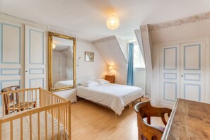 Un dormitorio con una cama, una silla de madera, una cuna y un espejo.