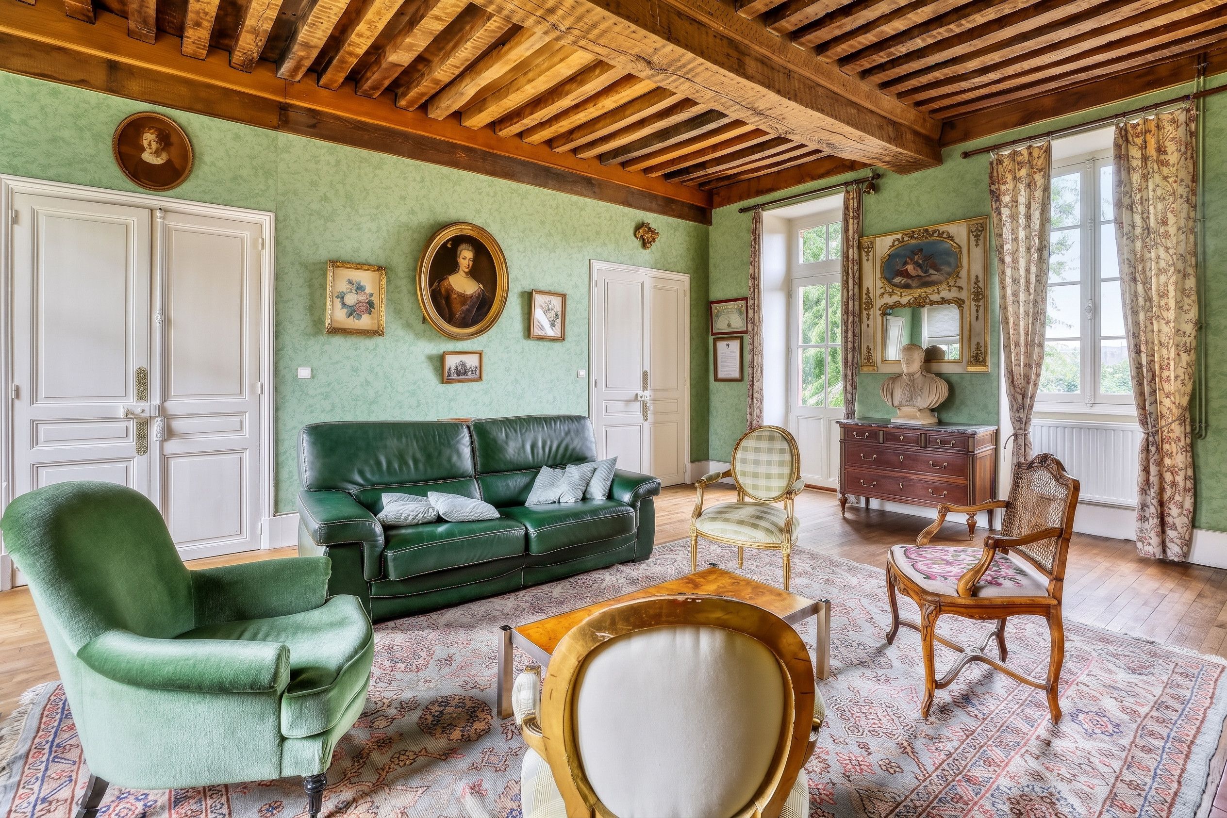 Une pièce avec un canapé vert, un fauteuil vert, une table basse en bois et un tapis à motifs.