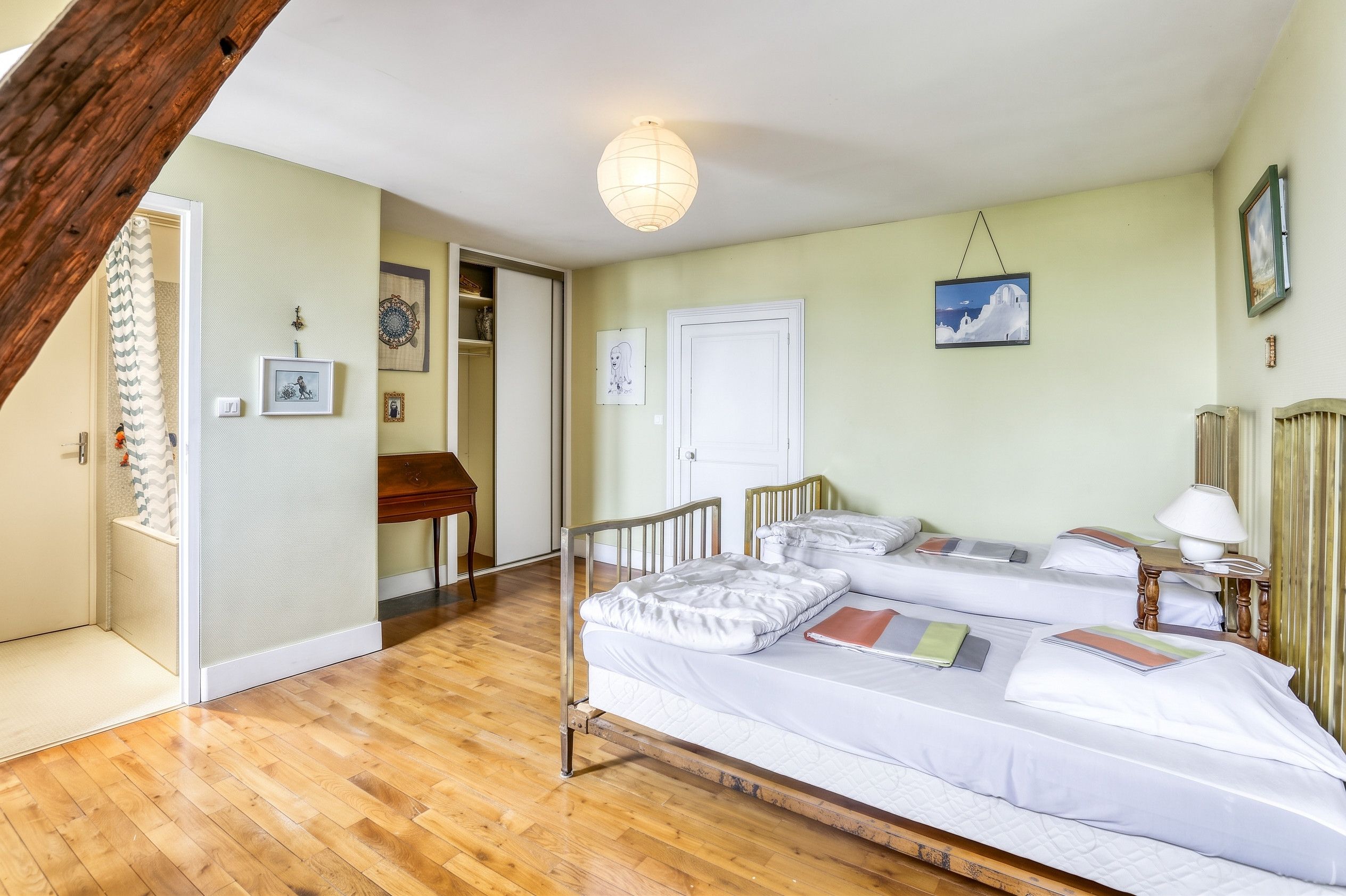 Une chambre avec deux lits, un plancher en bois, une porte blanche et un luminaire suspendu.