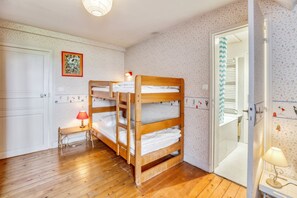 Een slaapkamer met een stapelbed, een klein tafeltje en een lamp, een deur met spiegel en behang met een patroon.
