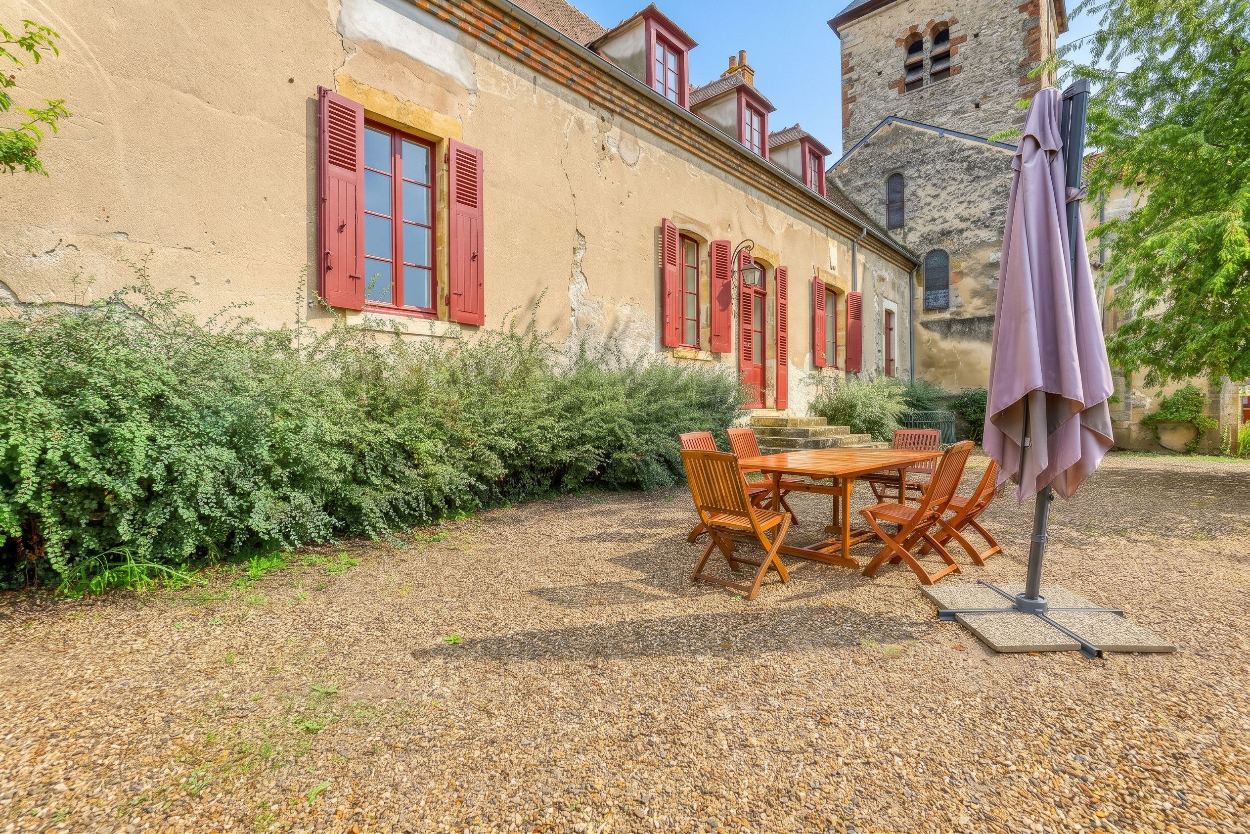 A rustic building with a gravel patio, wooden furniture, and red shutters.