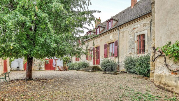 Une cour avec un arbre, un bâtiment aux volets rouges et un chemin de gravier.