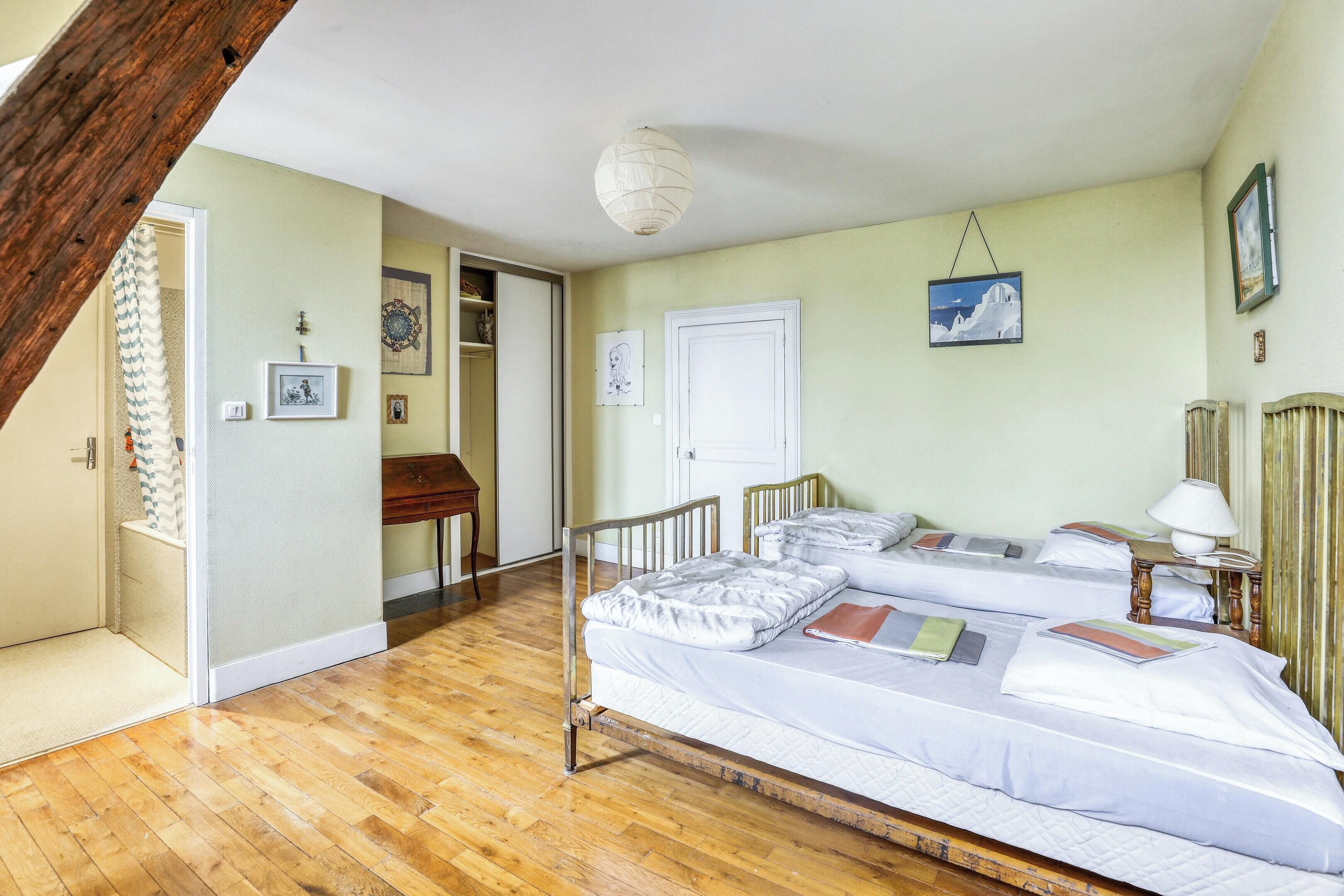 A room with two beds, wooden flooring, a white ceiling, and a hanging light fixture.