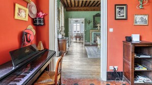 Une pièce comprenant un piano, une table à manger et des chaises. Un couloir mène à une autre pièce.