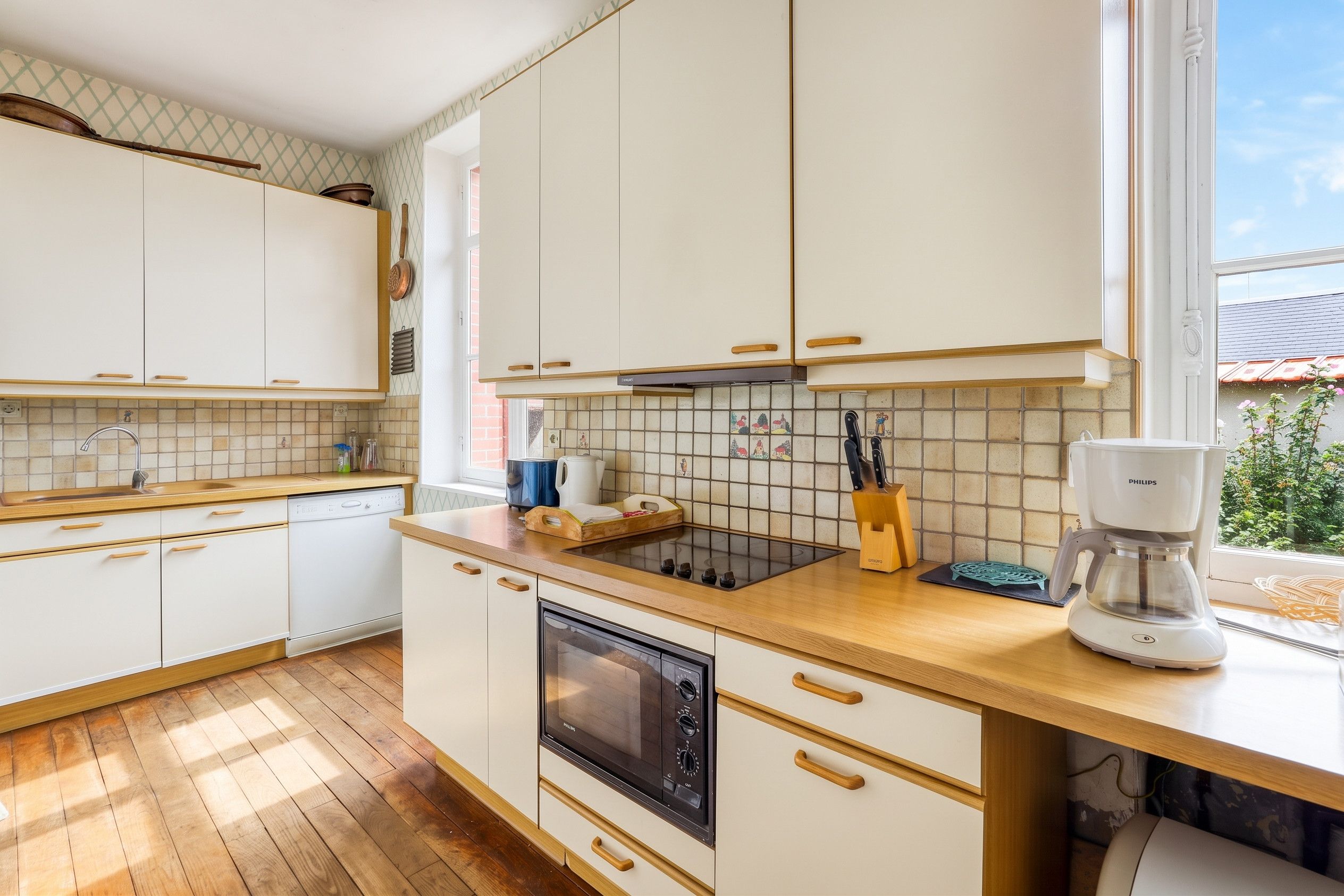 Een moderne keuken met witte kasten, een houten aanrecht, een inbouwoven en een koffiezetapparaat.