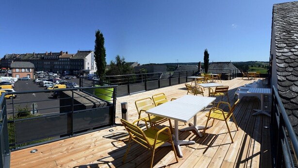 Terraço no telhado com piso de madeira, cadeiras amarelas e uma mesa.