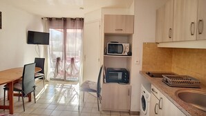 Una cocina compacta con microondas, tostadora y lavadora, una zona de comedor con mesa y sillas, y un televisor montado en la pared.