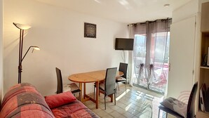 Una habitación con cama, una mesa, sillas, televisión y ventana con cortinas.